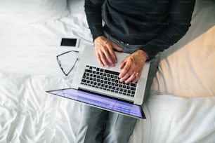 Homme d’affaires mature avec ordinateur portable et smartphone dans une chambre d’hôtel. Homme méconnaissable travaillant sur un ordinateur.