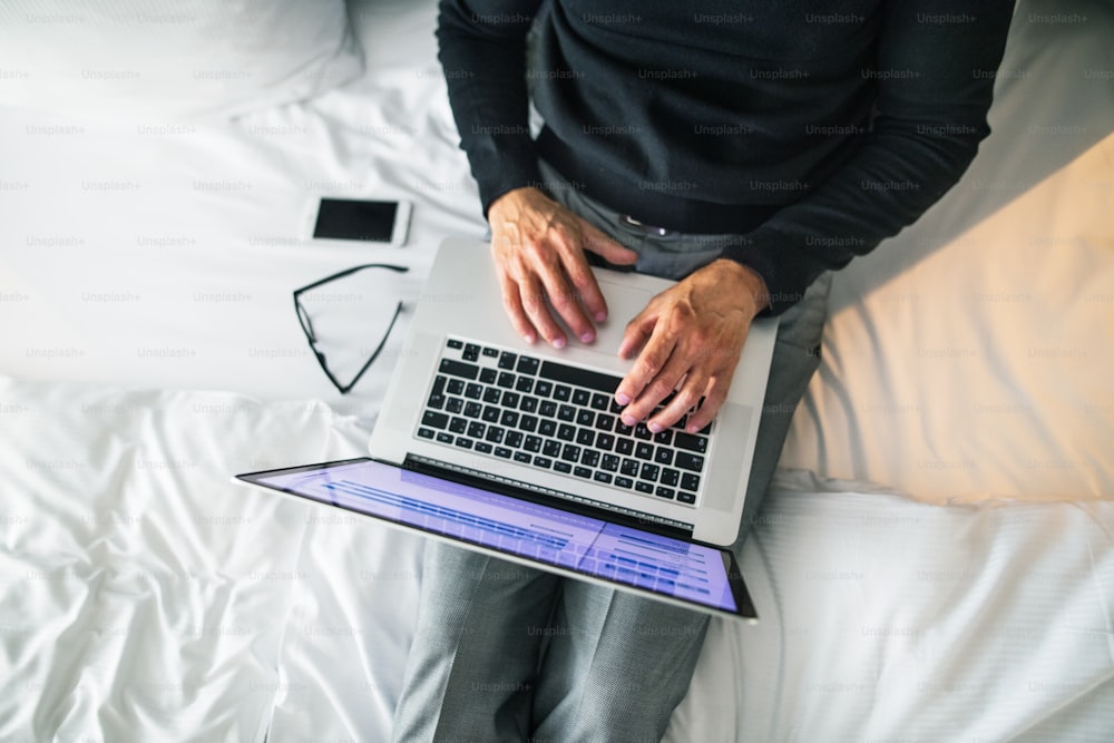 Mature businessman with laptop and smartphone in a hotel room. Unrecognizable man working on a computer.