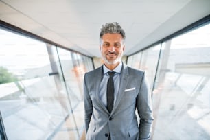 Handsome mature businessman walking in the corridor, travelling.Mature businessman with smartphone walking in the corridor, travelling.