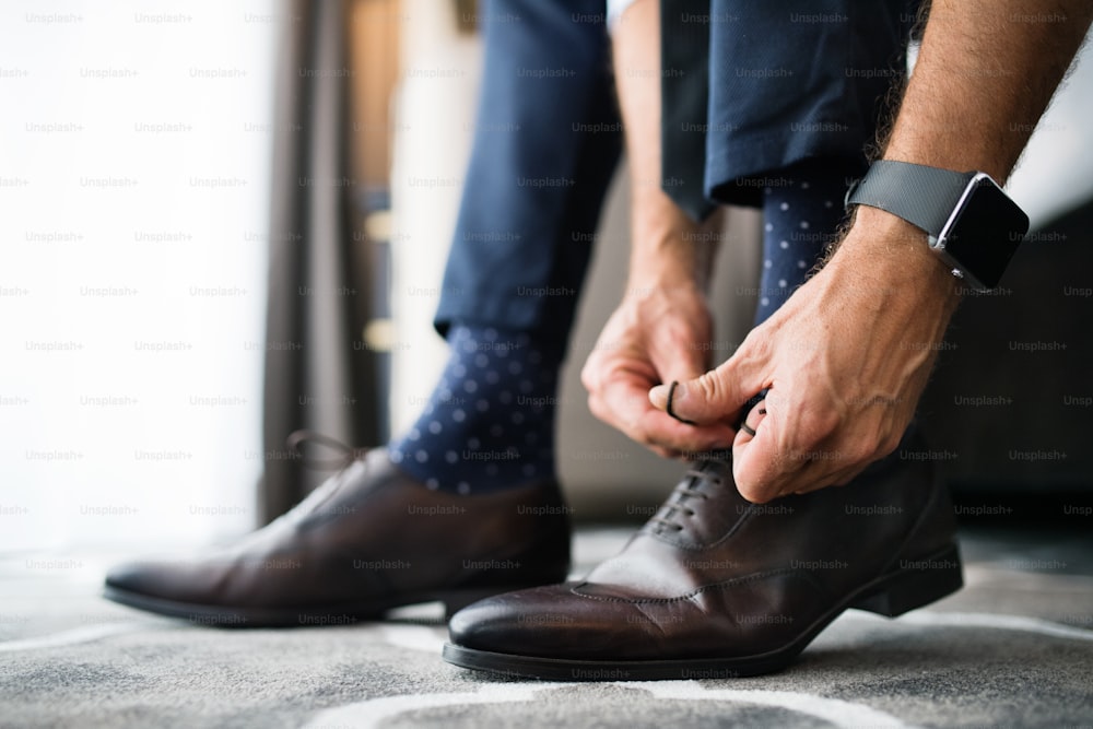 Uomo d'affari irriconoscibile che si veste in una stanza d'albergo. Uomo che si allaccia i lacci delle scarpe. Primo piano.