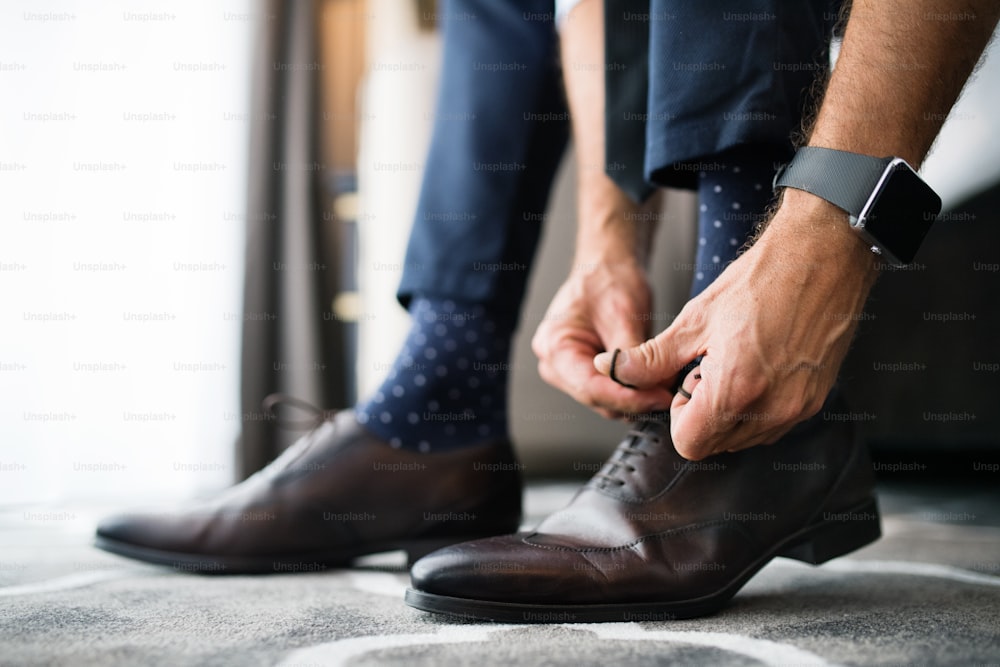 Unrecognizable businessman dressing up in a hotel room. Man tying his shoelaces. Close up.