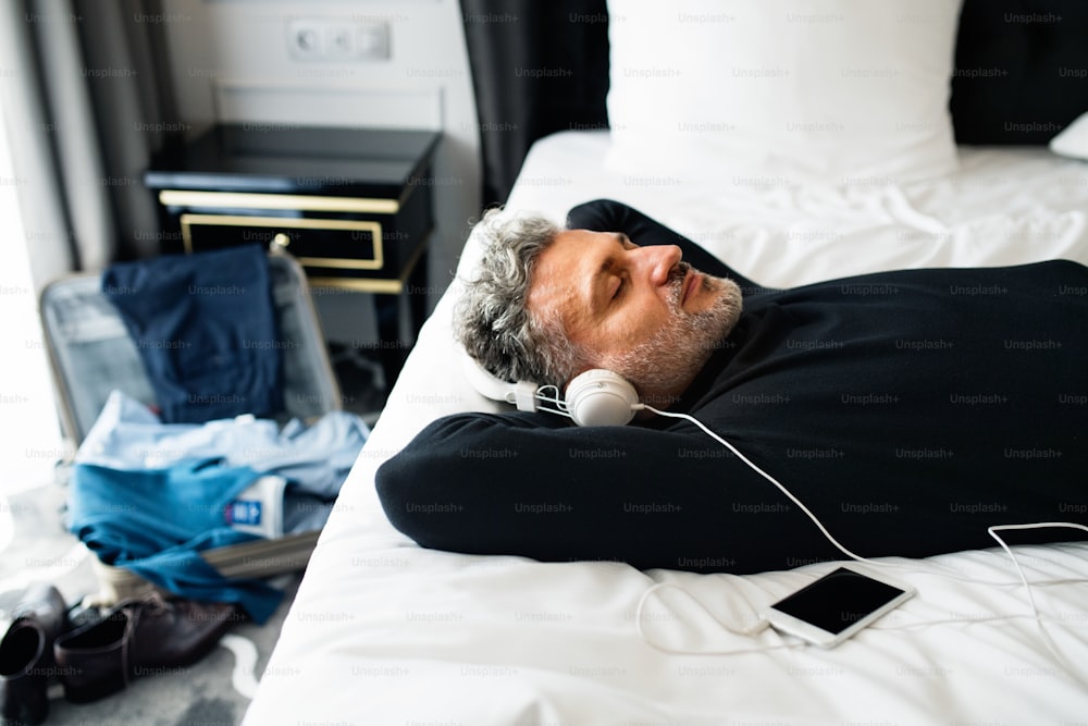 Mature businessman with a smartphone in a hotel room. Handsome man with headphones listening to music.