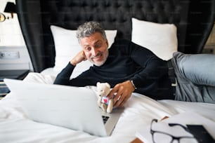 Empresário maduro com laptop em um quarto de hotel. Homem bonito usando telefonema on-line e vídeo.