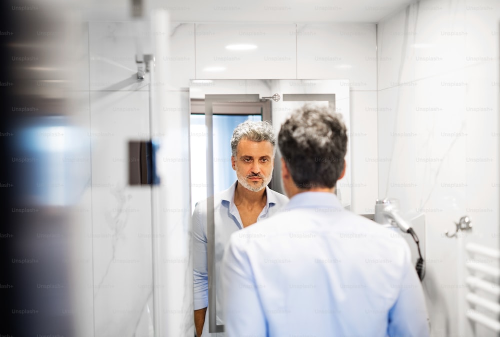 Mature businessman in a hotel room bathroom. Handsome man looking in the mirror.