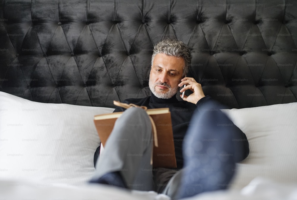 Uomo d'affari maturo con smartphone in una stanza d'albergo. Bel uomo che fa una telefonata.