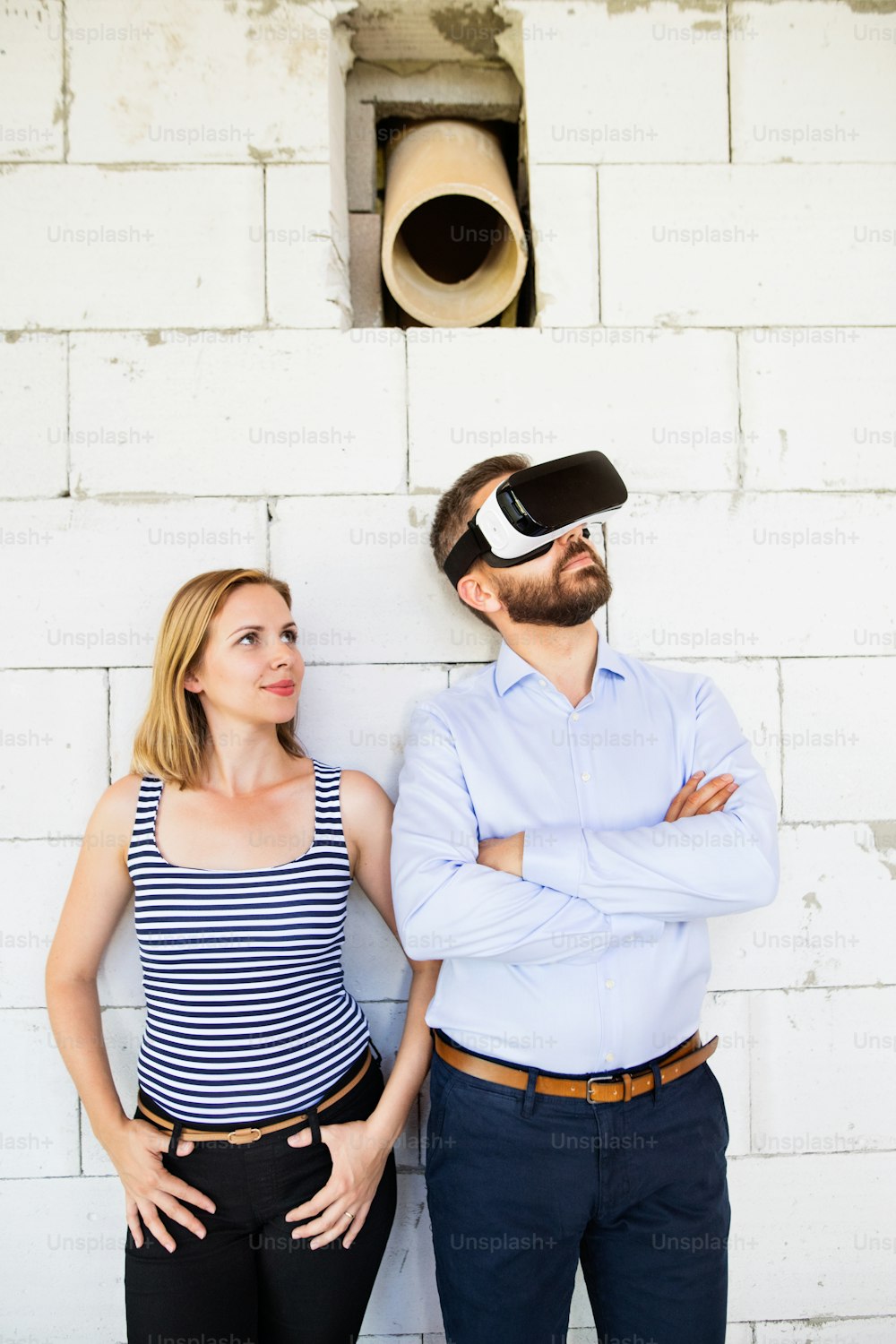 Young married couple or architects at the construction site. Man wearing virtual reality goggles.