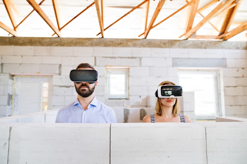 Jeune couple marié ou architectes avec des lunettes de réalité virtuelle sur le chantier.