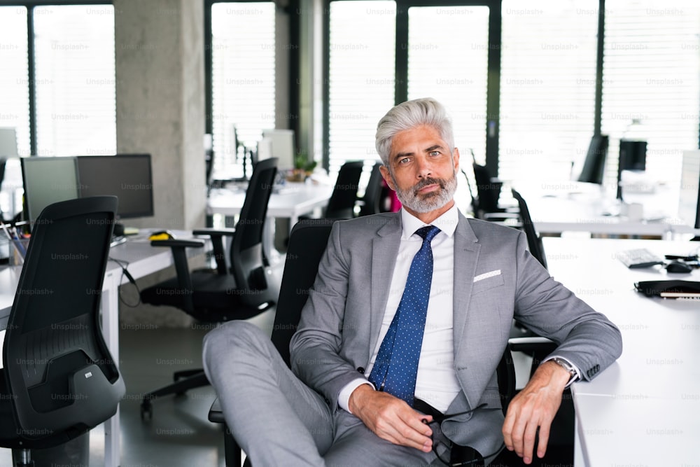 Hombre de negocios maduro con traje gris sentado en el escritorio de la oficina.