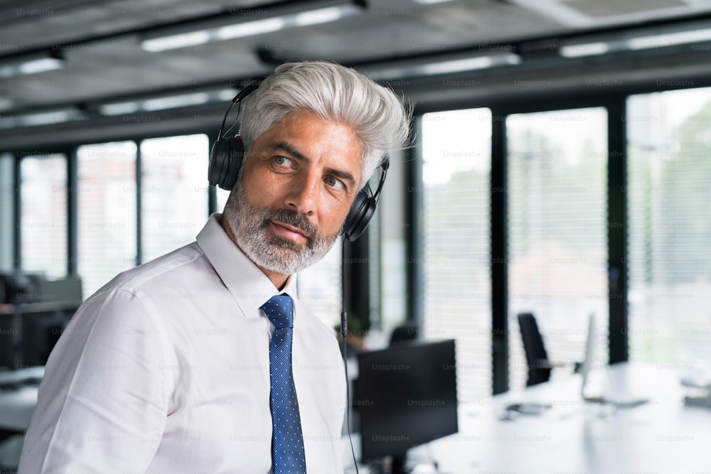 Mature businessman with headphones in the office listening to music.