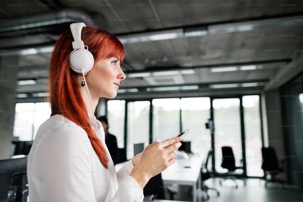 Beautiful young businesswoman with smartphone, wearing big white headphones.
