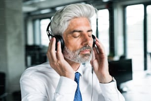 Mature businessman with headphones in the office listening to music.