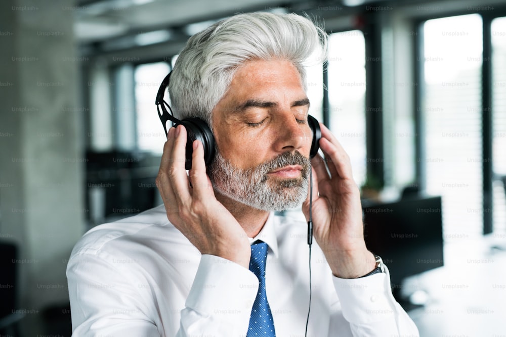 Uomo d'affari maturo con le cuffie in ufficio ad ascoltare musica.