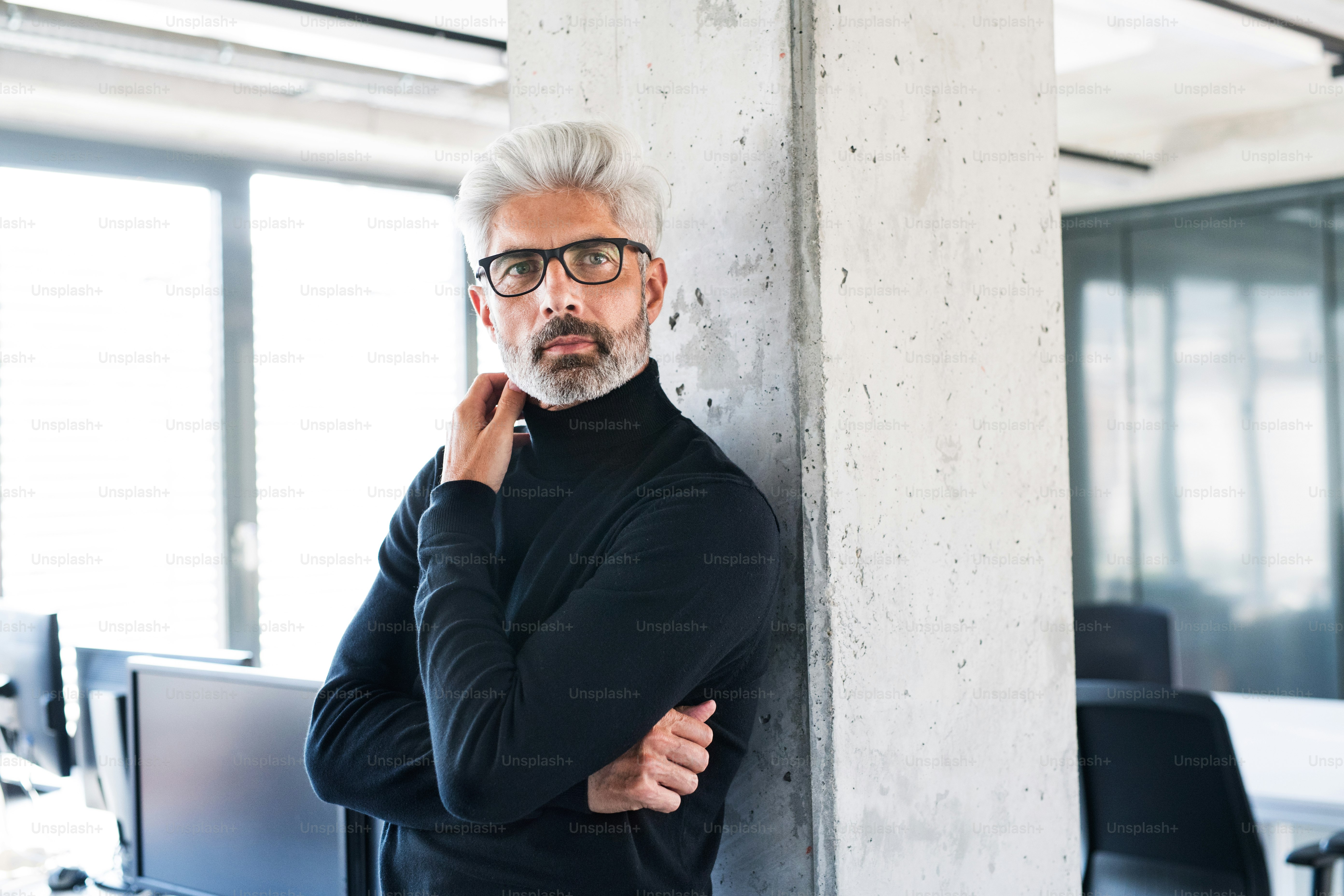 Handsome mature businessman with gray hair in black turtleneck and eyeglasses in the office