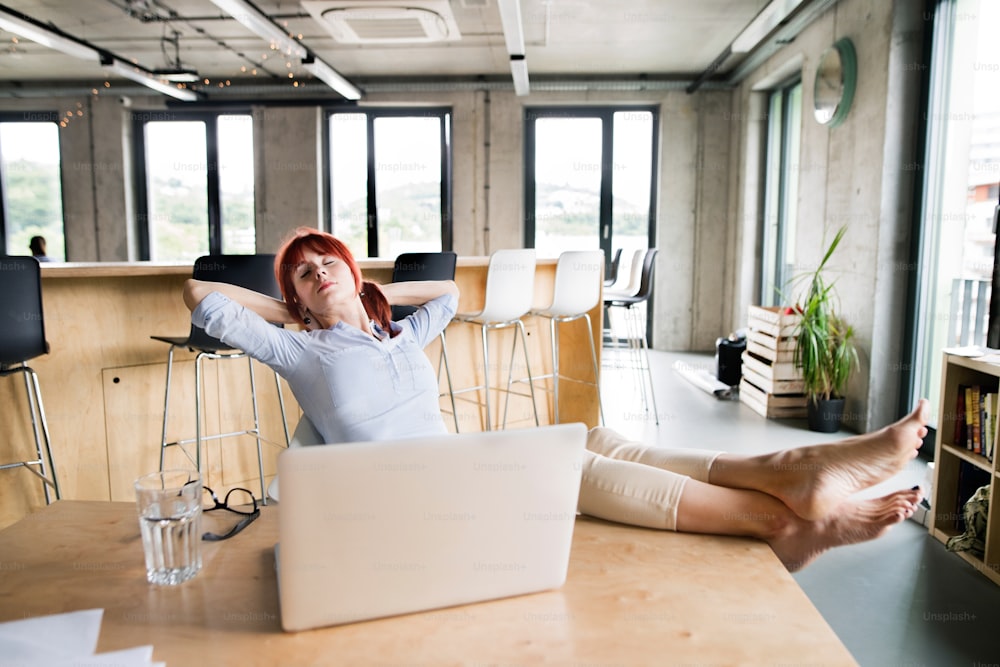 Bela empresária com laptop no escritório com os pés para cima na mesa.