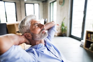 Thoughtful mature businessman with gray hair in the office wearing a blue shirt.