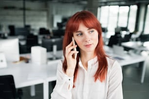 Beautiful young businesswoman with smart phone in her office making a phone call.
