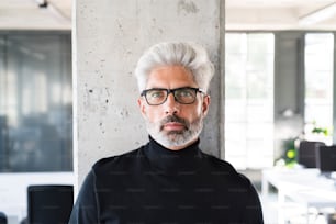 Handsome mature businessman with gray hair in black turtleneck and eyeglasses in the office.