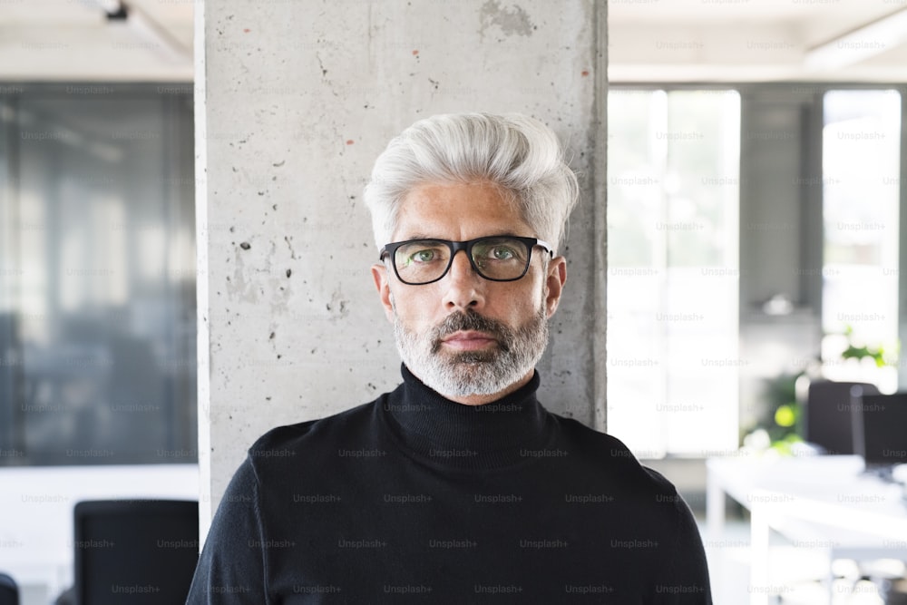 Handsome mature businessman with gray hair in black turtleneck and eyeglasses in the office.