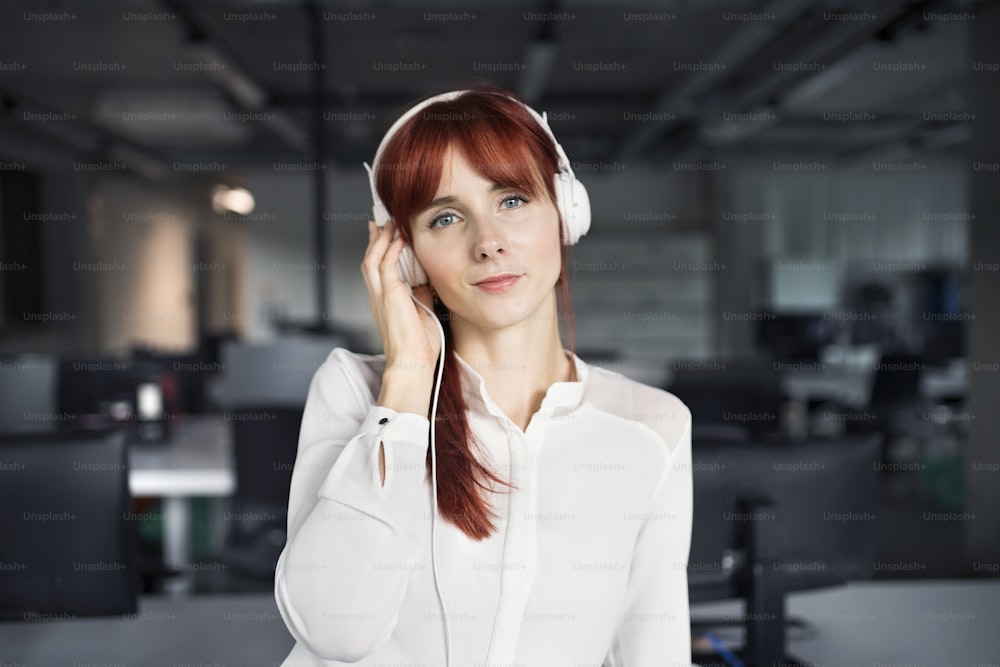 Beautiful young businesswoman in her office wearing big white headphones.