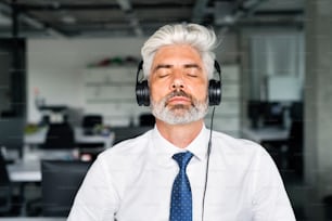 Mature businessman with headphones in the office listening music.