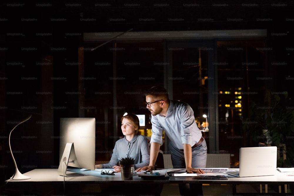 Two young businesspeople in the office at night working late, discussing a project.