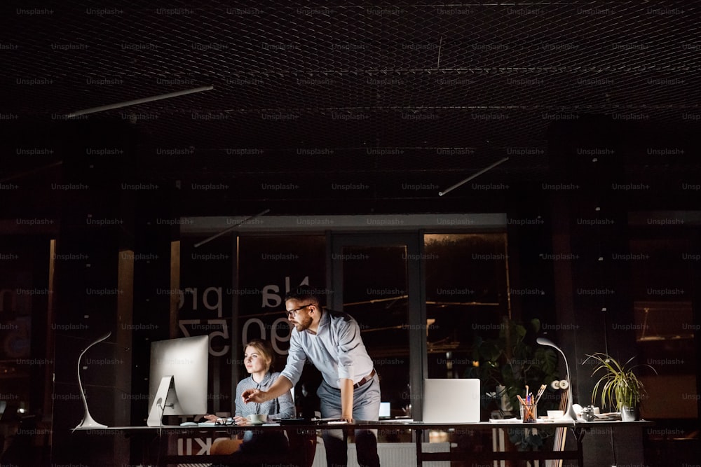 Two young businesspeople in the office at night working late, discussing a project.