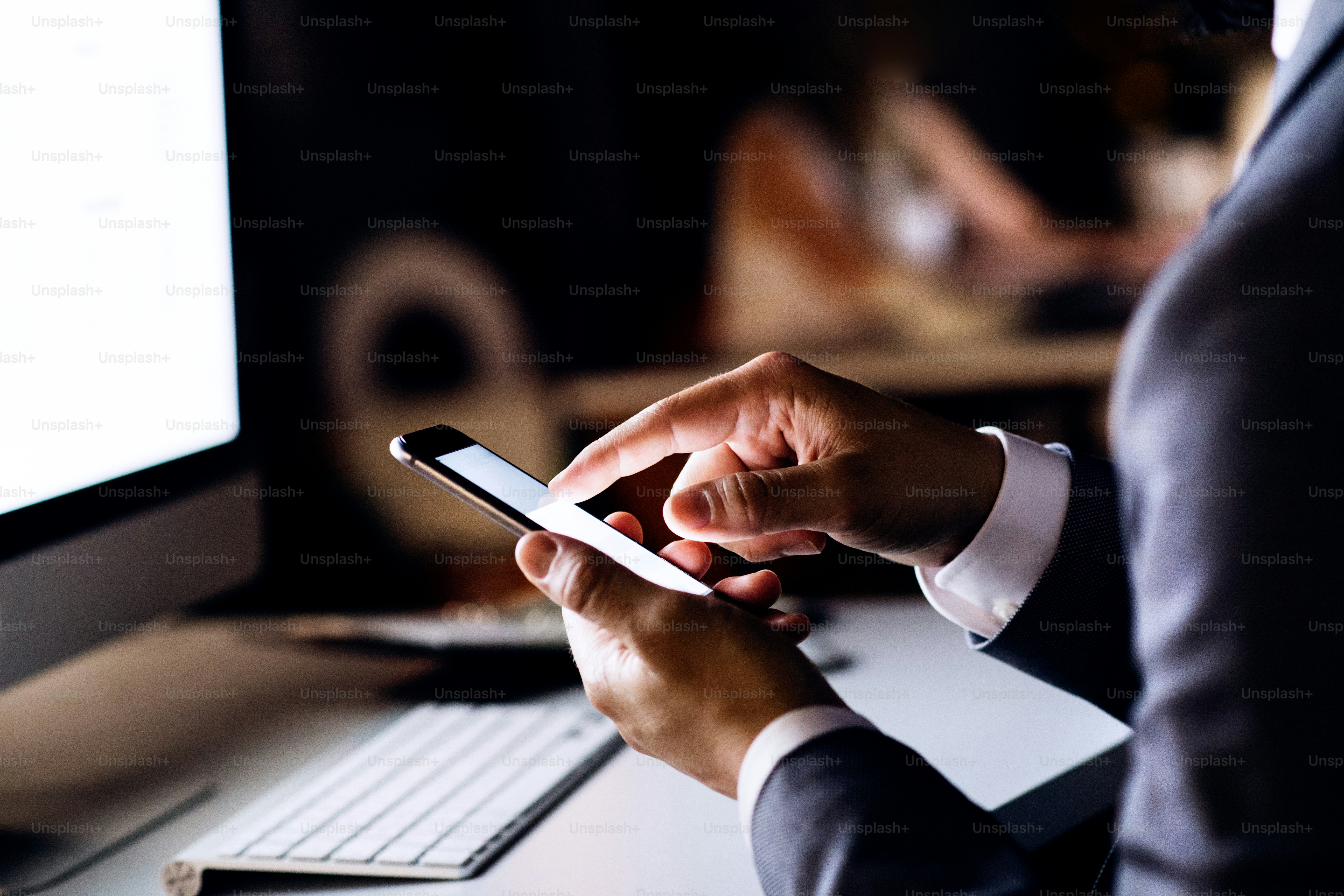 Empresário irreconhecível com smartphone em seu escritório trabalhando tarde da noite.