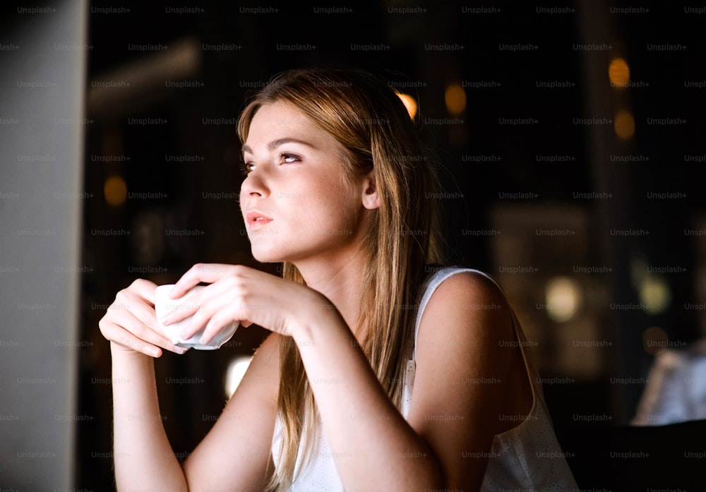 Beautiful young businesswoman in her office late at night working and drinking coffee.