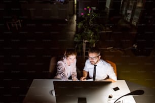 Due giovani imprenditori in ufficio di notte lavorano fino a tardi, discutendo di un progetto.