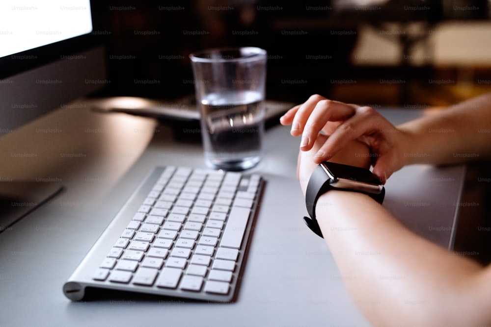 Unrecognizable businesswoman with computer in her office working late at night looking at smartwatch.