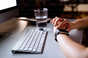 Donna d'affari irriconoscibile con il computer nel suo ufficio che lavora fino a tarda notte guardando smartwatch.