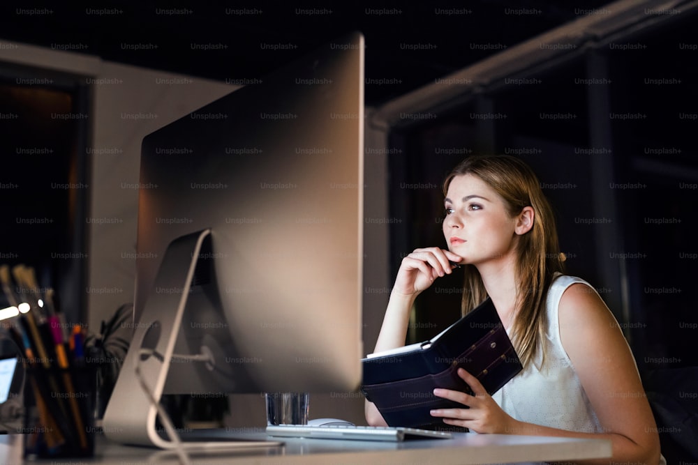 Schöne junge Geschäftsfrau im Büro in der Nacht, die spät arbeitet.