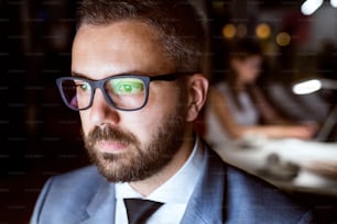 Giovane uomo d'affari hipster con occhiali neri nel suo ufficio a tarda notte, seduto alla scrivania.