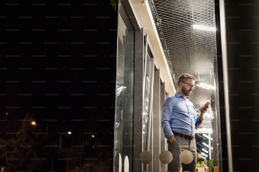 Hombre de negocios hipster reflexivo con teléfono inteligente en su oficina trabajando hasta altas horas de la noche.