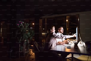 Two young businesspeople in the office at night working late, discussing a project.