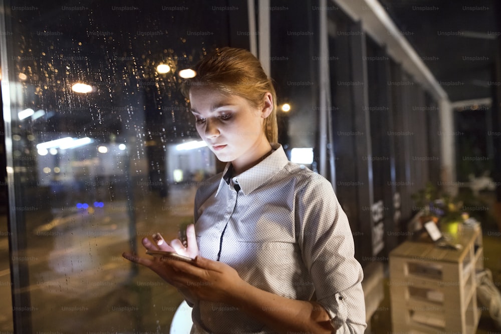 Beautiful young businesswoman with smart phone in the office working late at night.