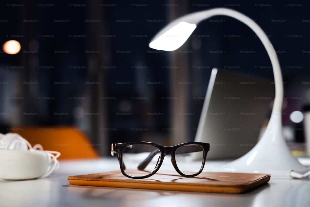 Office desk at night with eyeglasses, lamp and tablet. The interior of working office space.