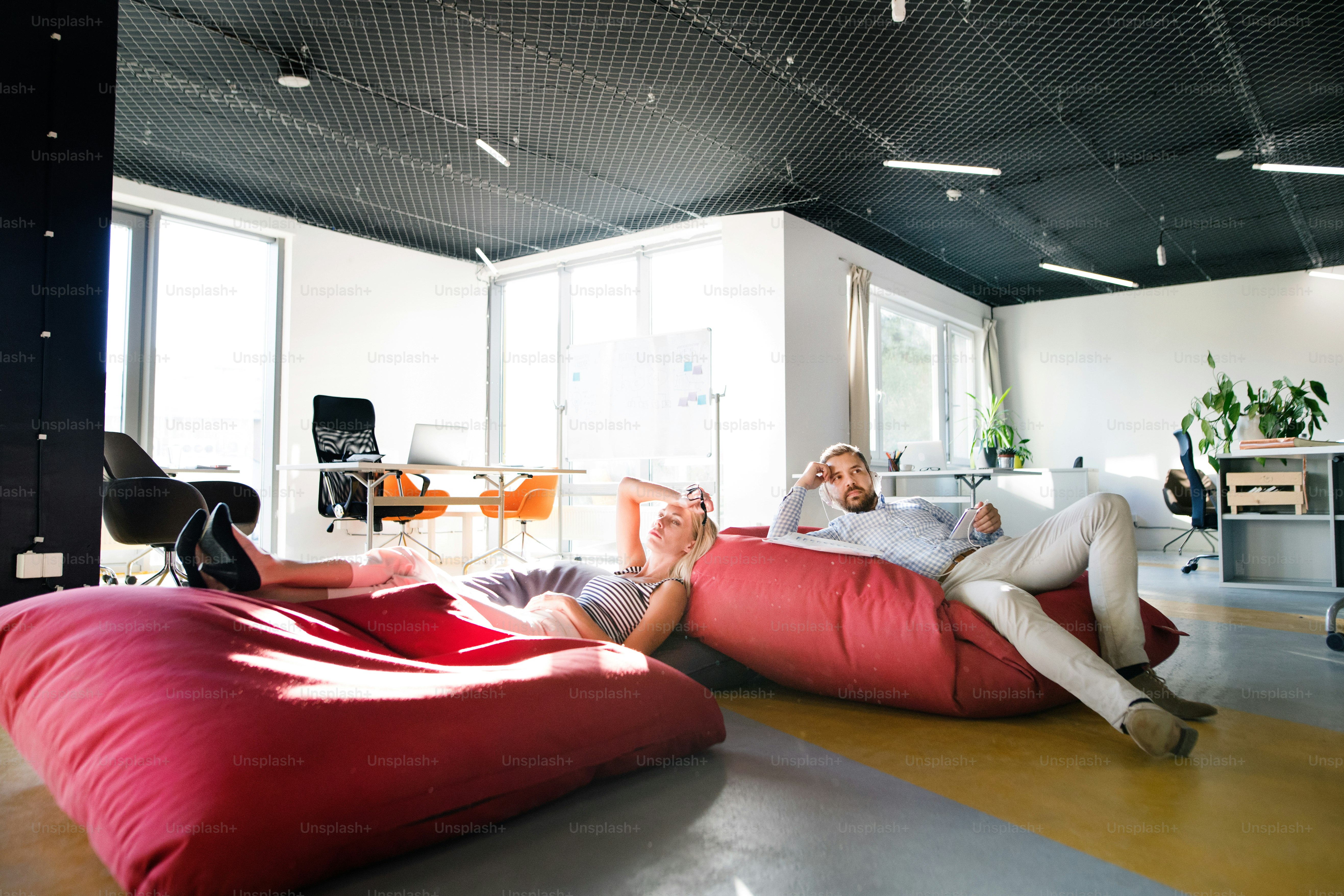 Young business people in the office sitting in bean bag chairs, relaxing.
