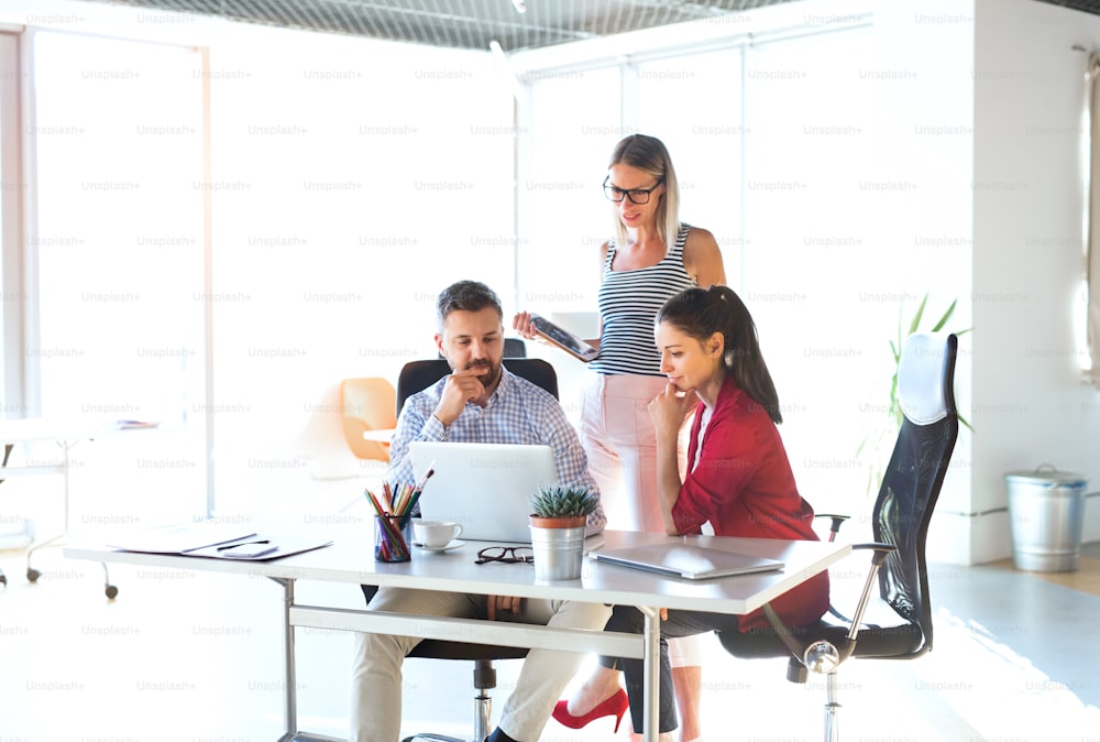 Three business people in the workplace. Two women and man sitting in the office working together, discussing a project.