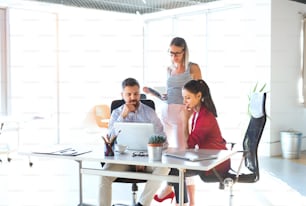 Three business people in the workplace. Two women and man sitting in the office working together, discussing a project.