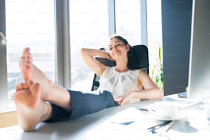 Beautiful young businesswoman in her office sitting with legs on desk.