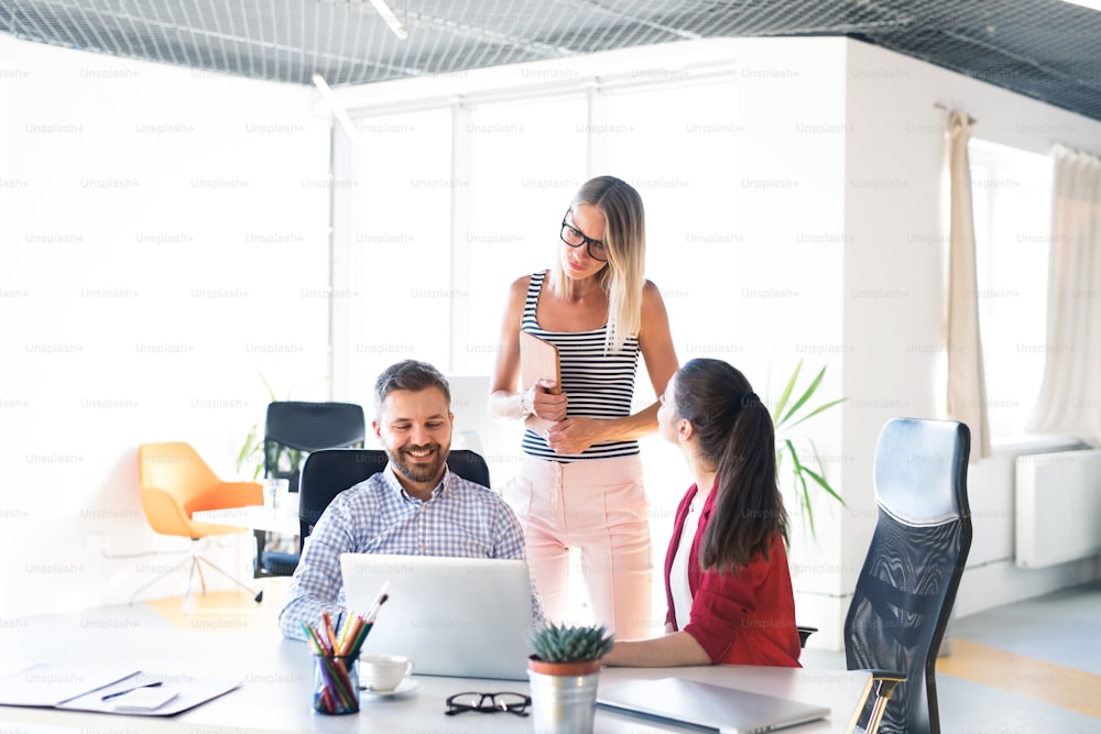 Tre uomini d'affari sul posto di lavoro. Due donne e un uomo in ufficio parlano insieme.