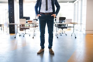 Unrecognizable young businessman standing in his office, hands in pockets.