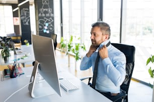 Handsome young businessman in his office, sitting at the desk, computer in front of him, adjusting his tie.