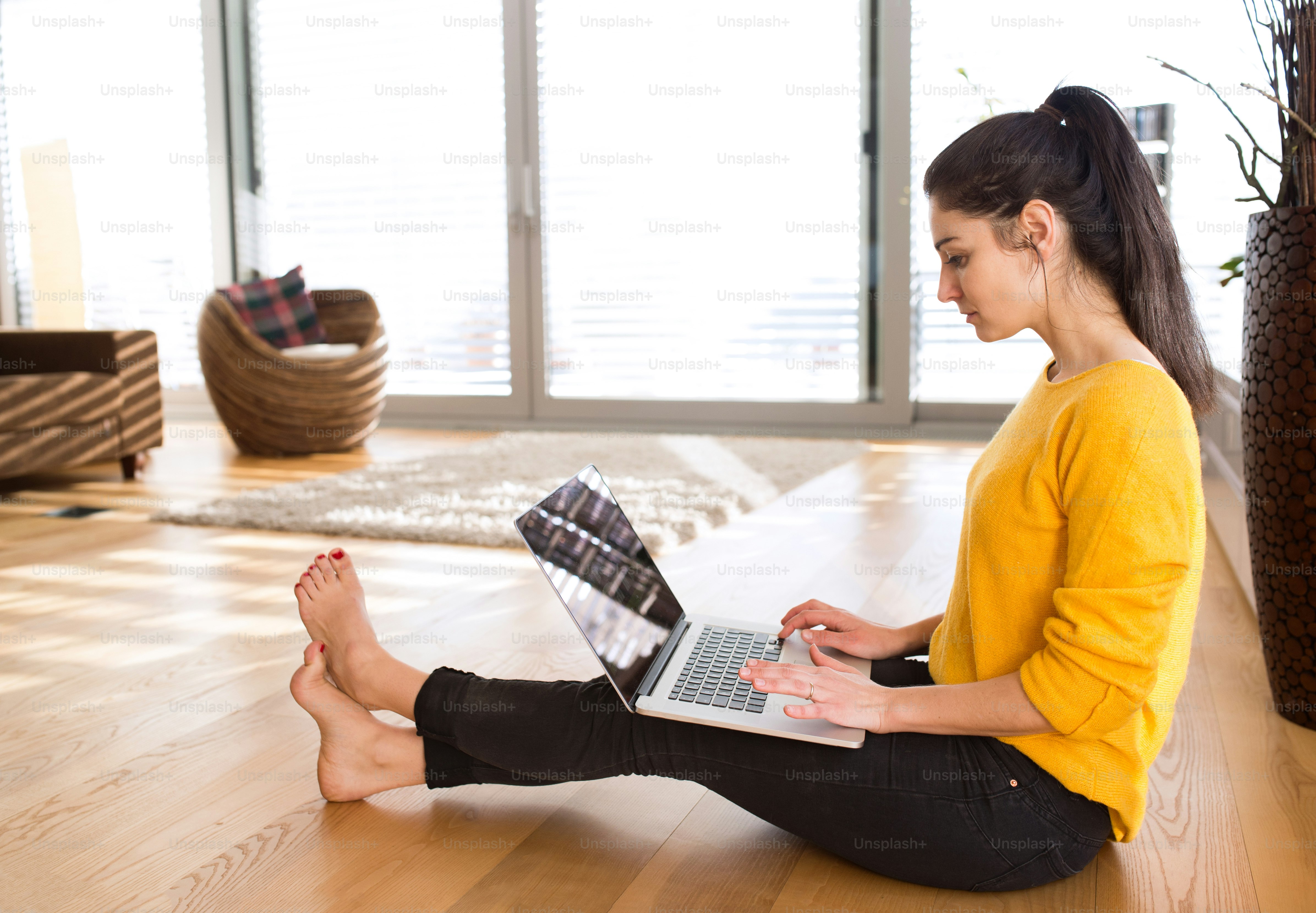 Beautiful young woman at home sitting on the floor, working on laptop, writing something