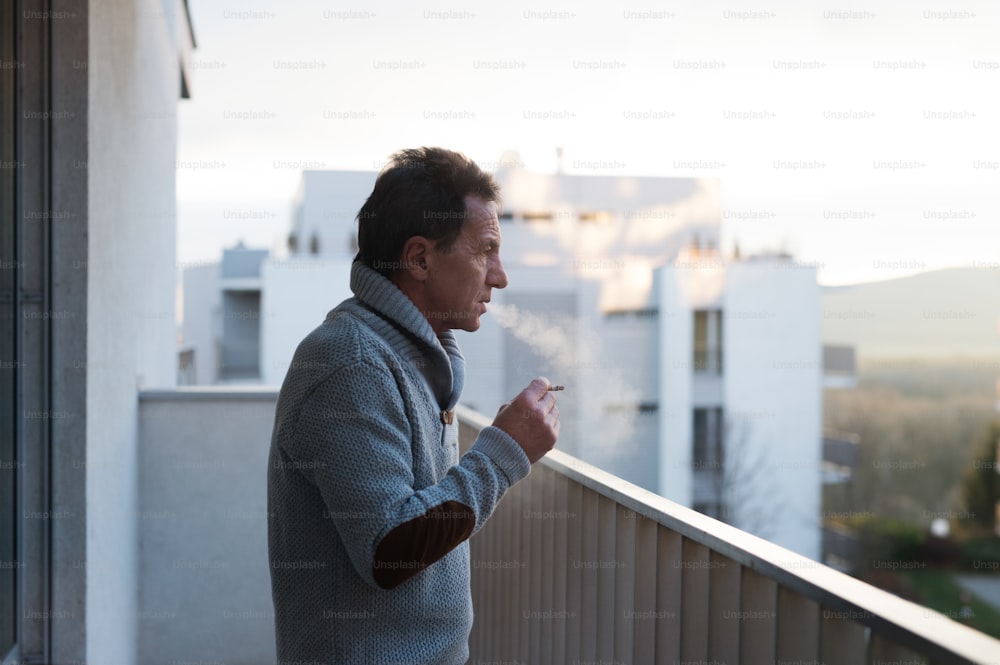 Ernster älterer Mann, der auf dem Balkon steht und eine Zigarette raucht