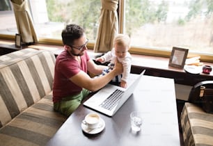 Young handsome man with notebook in cafe sitting at the table drinking coffee, holding his son