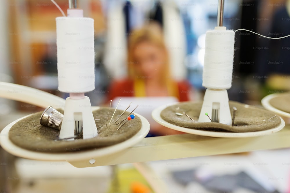 Close up of two white threads on sewing machine, pins and pin cushions