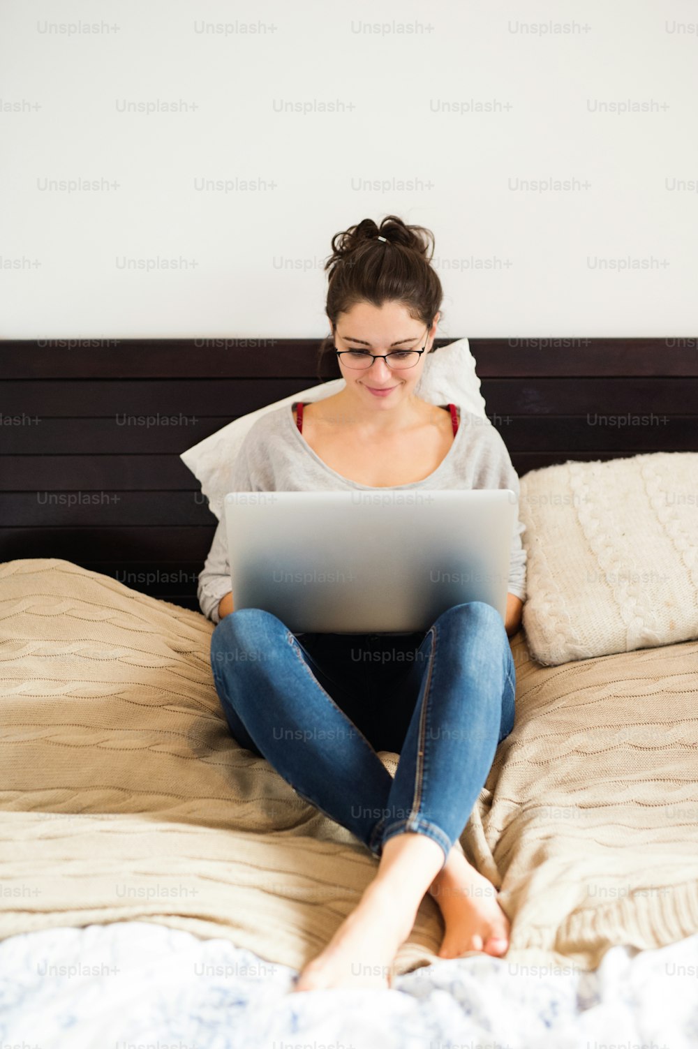 Beautiful young woman sitting on bed, working on notebook, home office.