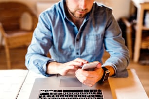 Hombre irreconocible sentado en el escritorio trabajando desde casa en la computadora y el teléfono inteligente